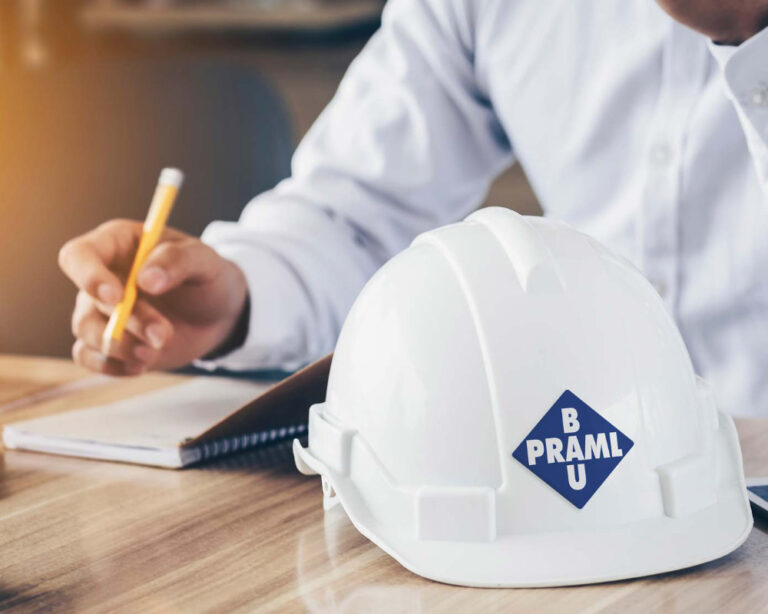 Helm mit Praml Bau Logo auf Schreibtisch vor Bewerbendem der Arbeitsvertrag unterschreibt